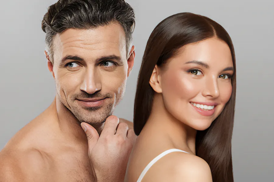 Aesthetics-Cosmetics-Doctor A handsome man and beautiful brunette woman stand against a gray background showing their smooth beautiful skin resulting from aesthetic and cosmetic care from Pierre Rojas, DO in South Lyon.