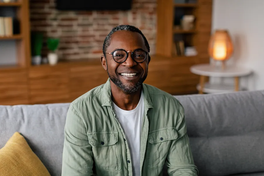 Andropause-Doctor A middle aged black man in a green button up shirt sits on his couch smiling, happy with his treatment for andropause and low testosterone from Pierre Rojas, DO in South Lyon.