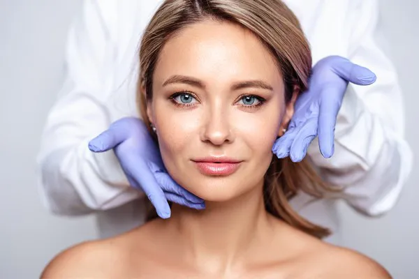 Botox-Doctor Close up of a woman's face with a doctor wearing rubber gloves standing behind her holding his hands around her face to show the amazing Botox Cosmetic treatment from Pierre Rojas, DO in South Lyon.