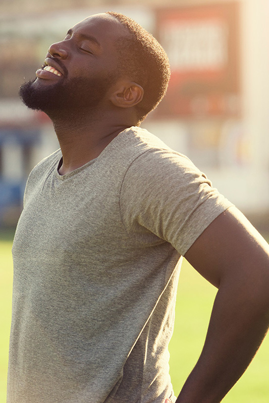 Lean-Muscle-and-Recovery-Treatment A black man in a gray t-shirt and smiles, looking up with closed eyes after a satisfying workout. Get treatment for lean muscle loss and recovery from Pierre Rojas, DO in South Lyon.