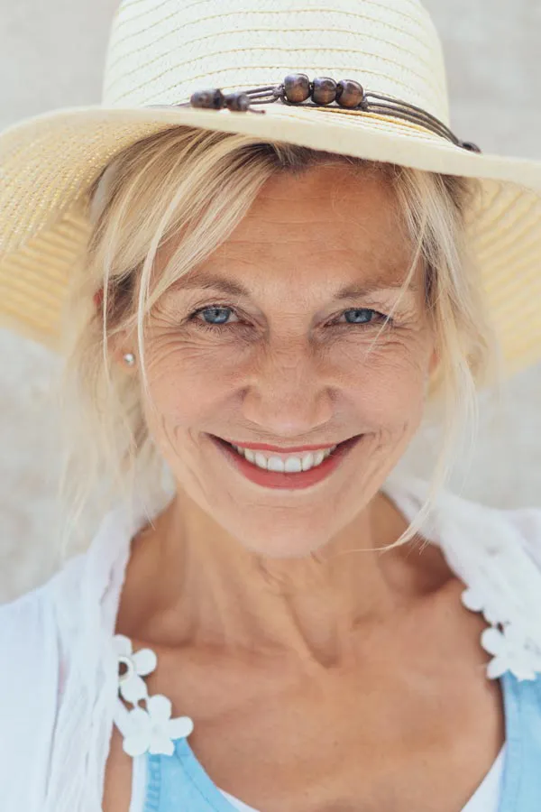 Menopause-Treatment A beautiful, smiling older woman with blonde hair and a sunhat, happy with menopause treatment from Pierre Rojas, DO in South Lyon.