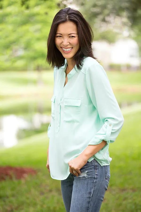 Perimenopause-Treatment A middle-aged brunette woman in a light green button-up shirt stands outside smiling, happy with her perimenopause treatment from Pierre Rojas, DO in South Lyon.