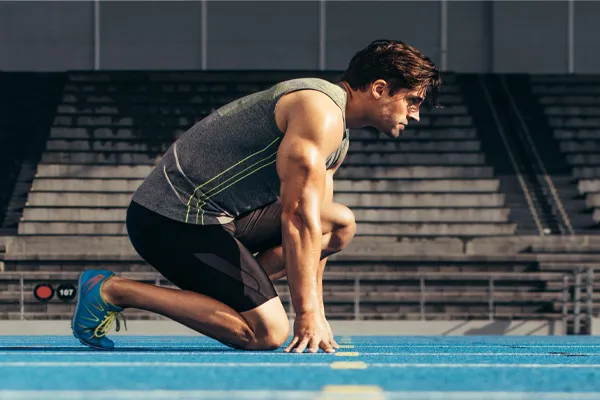 Sermorelin-Clinic With a determined look, Aamuscular man in track clothes kneels at the start of a race. Get Sermorelin peptide therapy from Pierre Rojas, DO in South Lyon.