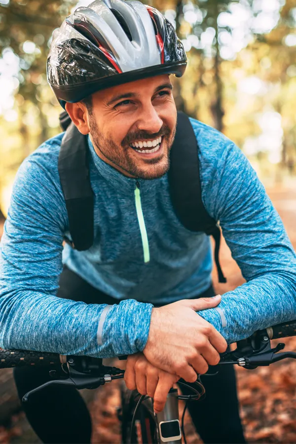 Testosterone-Low-T-Solutions-Treatment A middle-aged man on a trail in cycling clothes is smiling and leaning on his bike's handlebars. Get testosterone for Low T from Pierre Rojas, DO in South Lyon.