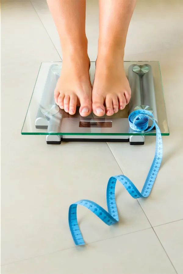 Weight-Loss-Resistance-Treatment Close-up of a woman's feet standing on a scale, with measuring tape by her toes, getting treatment for weight loss resistance from Pierre Rojas, DO in South Lyon.