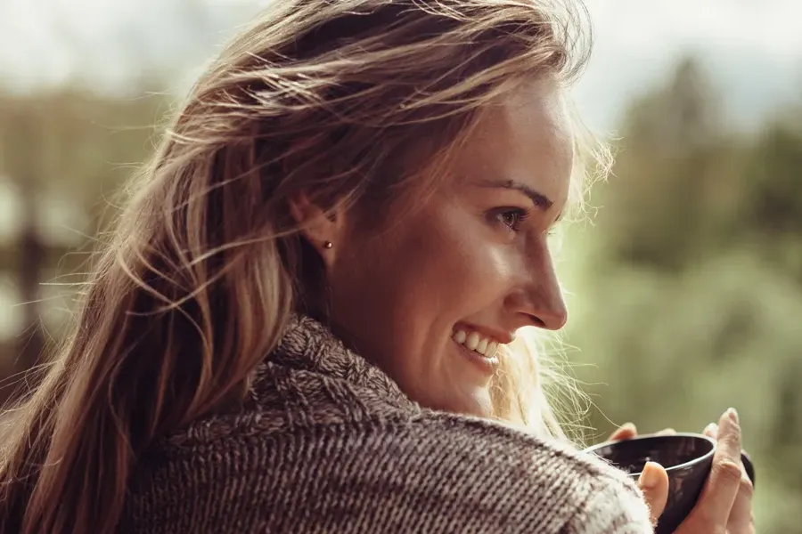 Womens-Health-Clinic A woman in a sweater looks out at the morning forest and smiles. Visit Women's Health expert Pierre Rojas, DO in South Lyon.
